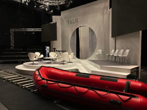 Backstage-Ansicht des Bühnenbilds mit Talkshow-Setting, Bühnentechnik und großem Rettungsboot in John Adams' The Death of Klinghoffer.